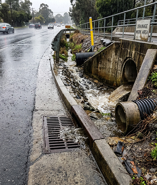 floods rushing in to a drain on a street